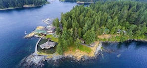 An aerial view of a small island with a dock, a building with a green roof, and dense forestation.