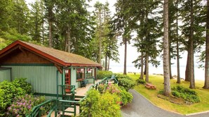 A lodge with a wooden exterior, a porch with chairs, and a view of the forest and water. - April Point Resort  (Quadra Island)