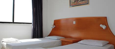 A hotel room with two single beds, a wooden headboard, a small bedside table, and a painting on the wall.