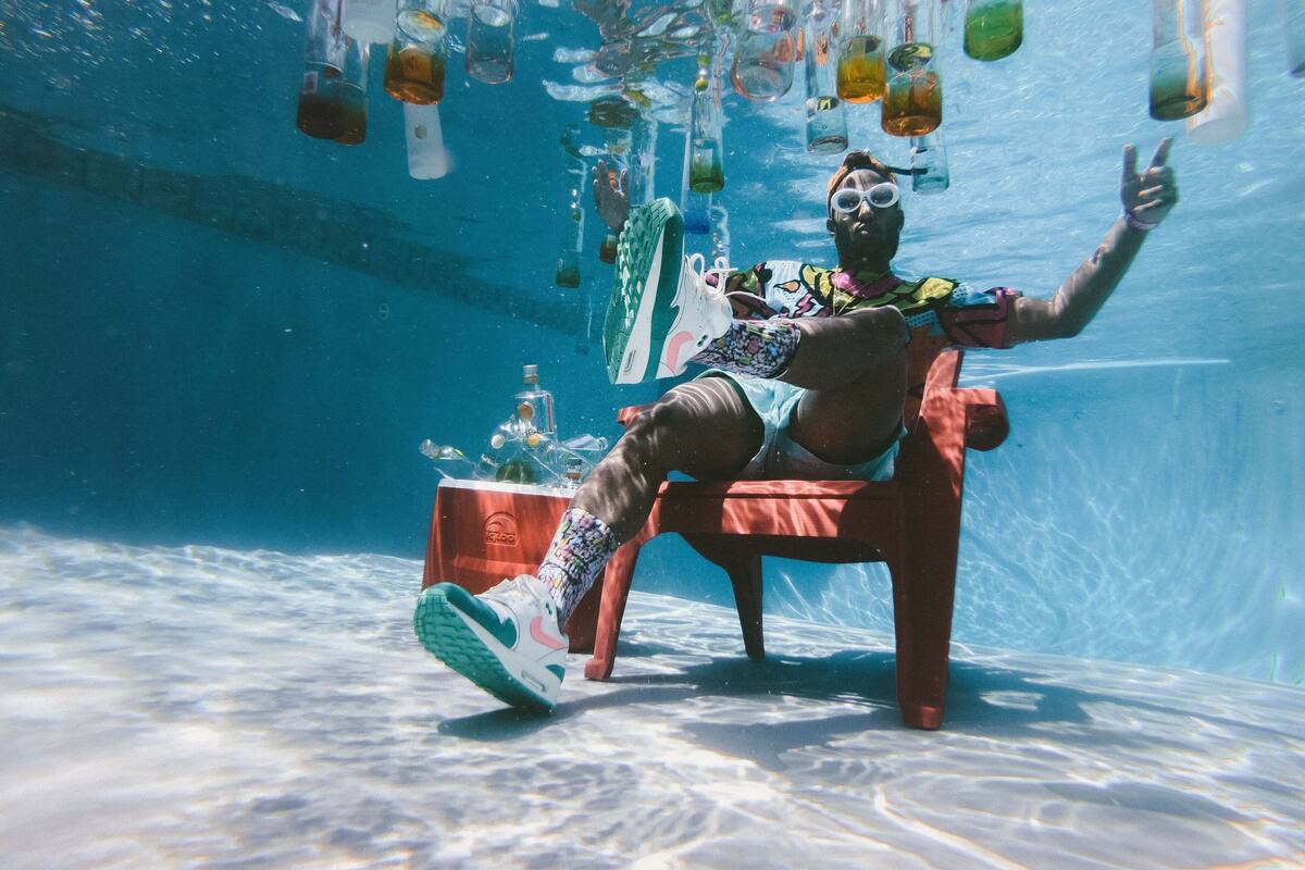 A person sitting on a chair underwater with various bottles and objects floating around.