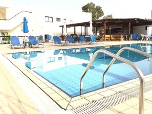 A swimming pool with blue tiles, surrounded by lounge chairs and umbrellas. - Florea Hotel Apartments (Ayia Napa)