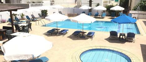 A pool area with lounge chairs and umbrellas, surrounded by buildings.