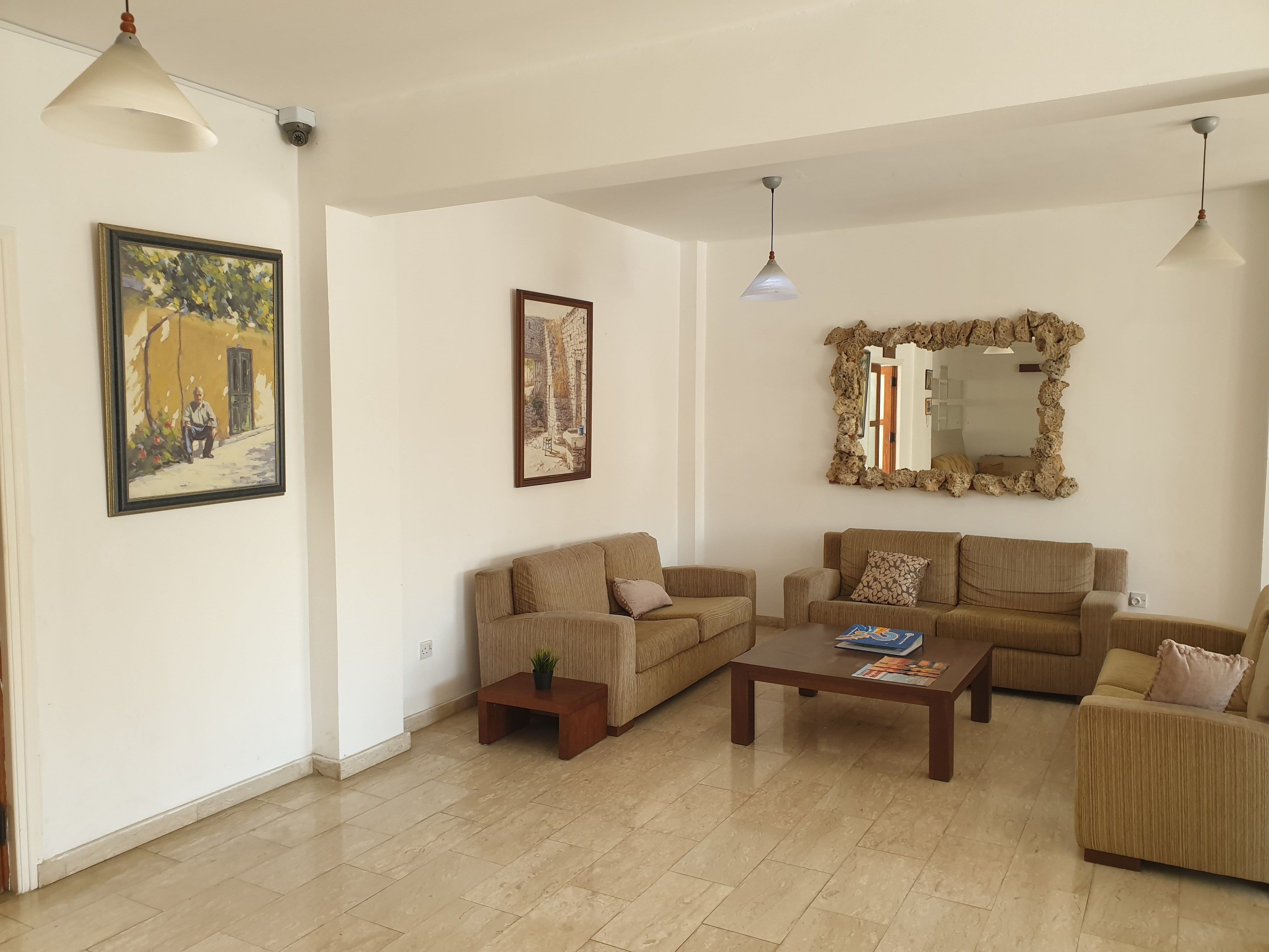 Amplia sala de estar con piso de baldosas color beige, dos sofás color beige, una mesa de centro y un espejo grande con marco natural.
