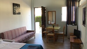 Une chambre d’hôtel comprenant un lit, un canapé, une table à manger avec des chaises, une télévision et une fenêtre avec des rideaux.