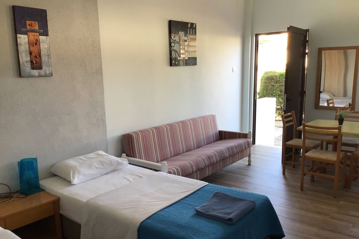 A hotel room with a bed, a sofa, a dining table with chairs, and artwork on the walls.