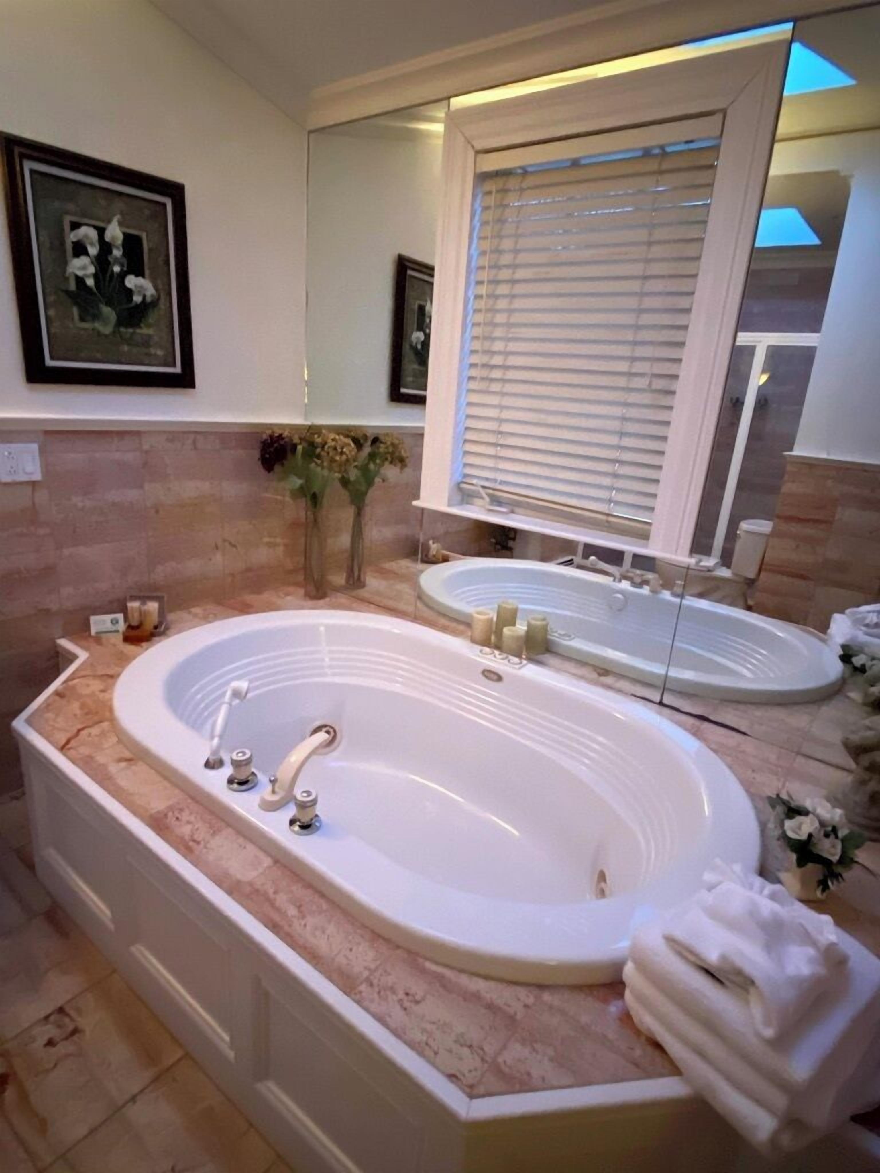 A bathroom with a large freestanding bathtub, a vanity with a mirror, and a window with blinds.
