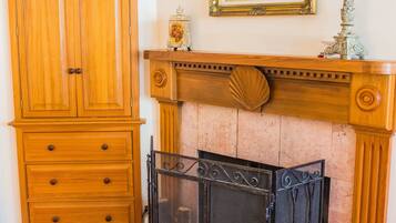 A room with a wooden wardrobe, a fireplace with a screen, and a framed painting on the wall.