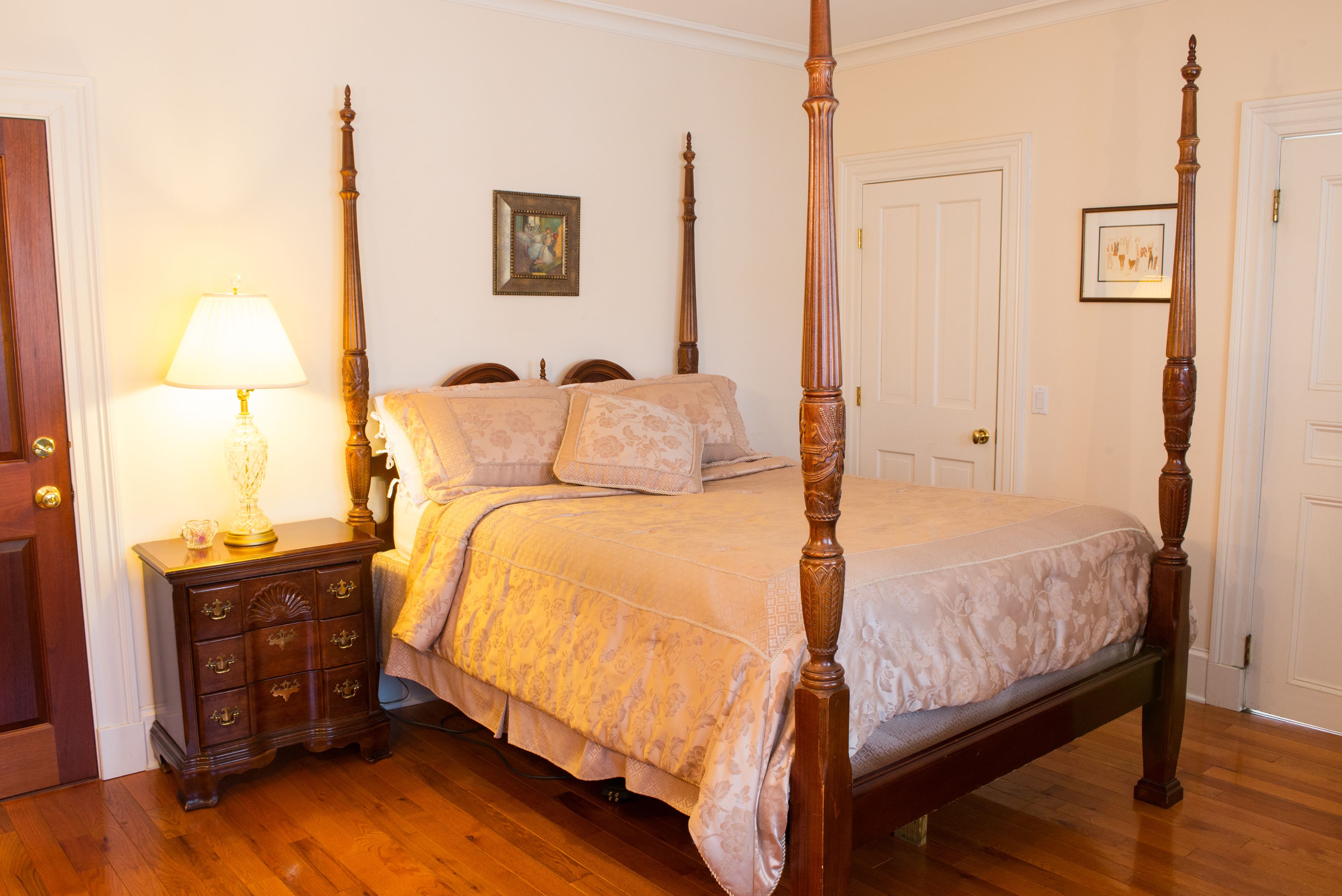 A four-poster bed with a wooden frame, a nightstand with a lamp, and a dresser with drawers.