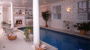 A pool area with a tiled deck, a seating area with a chair and a basket, and a potted plant. - Chiltern Inn (Bar Harbor)