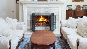 A room with a fireplace, two sofas, a coffee table, a chandelier, and a framed picture on the wall. - Chiltern Inn (Bar Harbor)