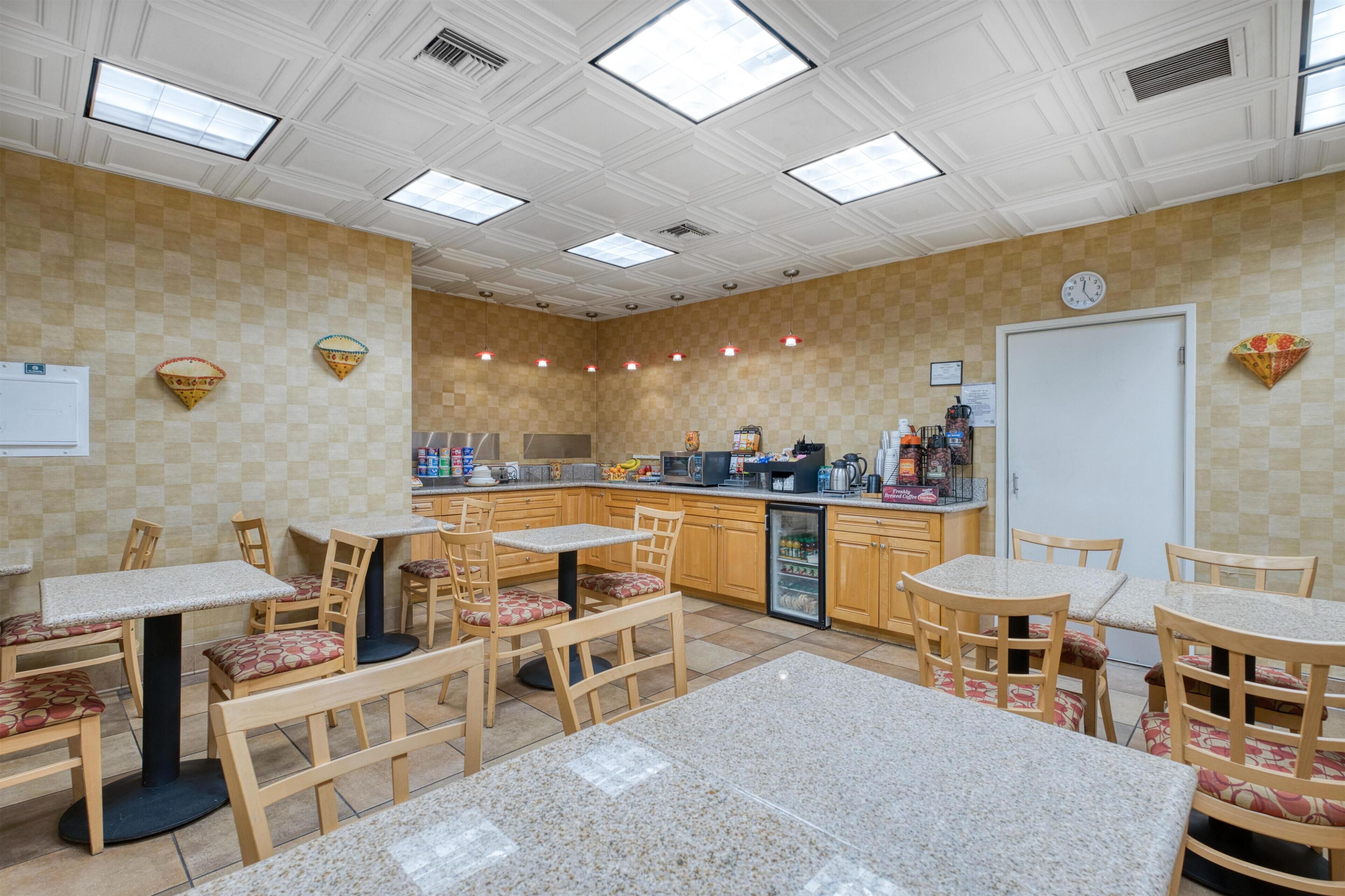A restaurant with checkered walls, wooden tables and chairs, a refrigerator, and a clock on the wall.