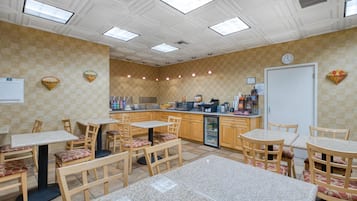A restaurant with checkered walls, wooden tables and chairs, a refrigerator, and a clock on the wall.