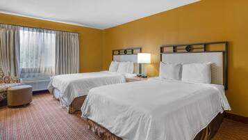 Habitación de hotel con dos camas, una ventana con cortinas, un pequeño sofá y suelo cubierto de alfombra.