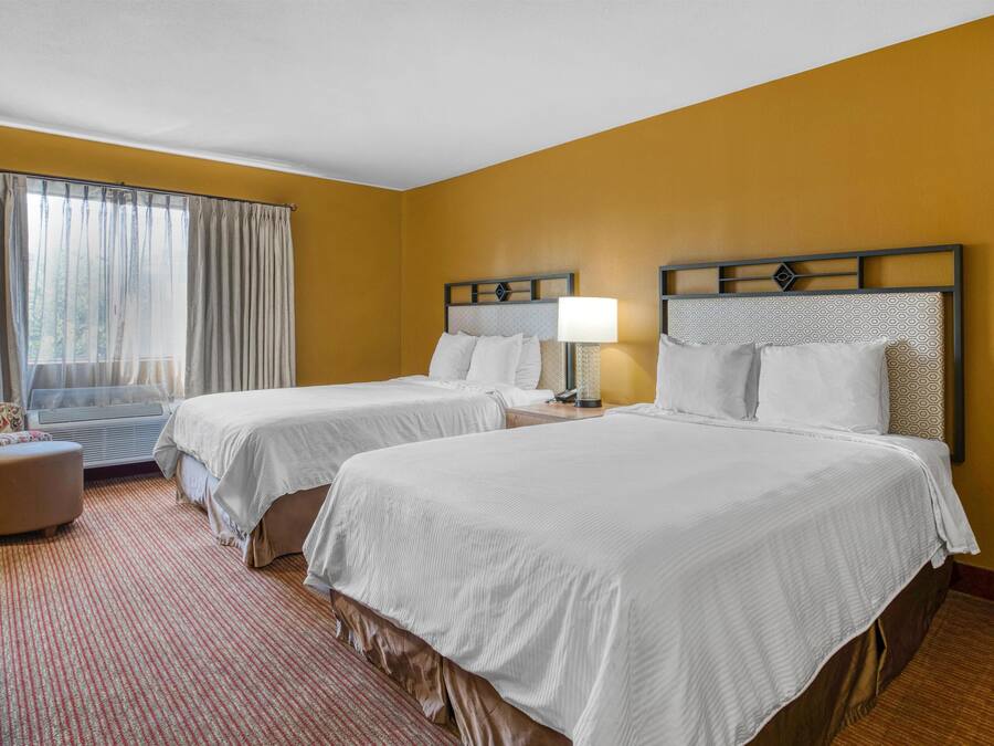 Hotelkamer met twee bedden, een raam met gordijnen, een kleine zithoek en een vloerbedekking.