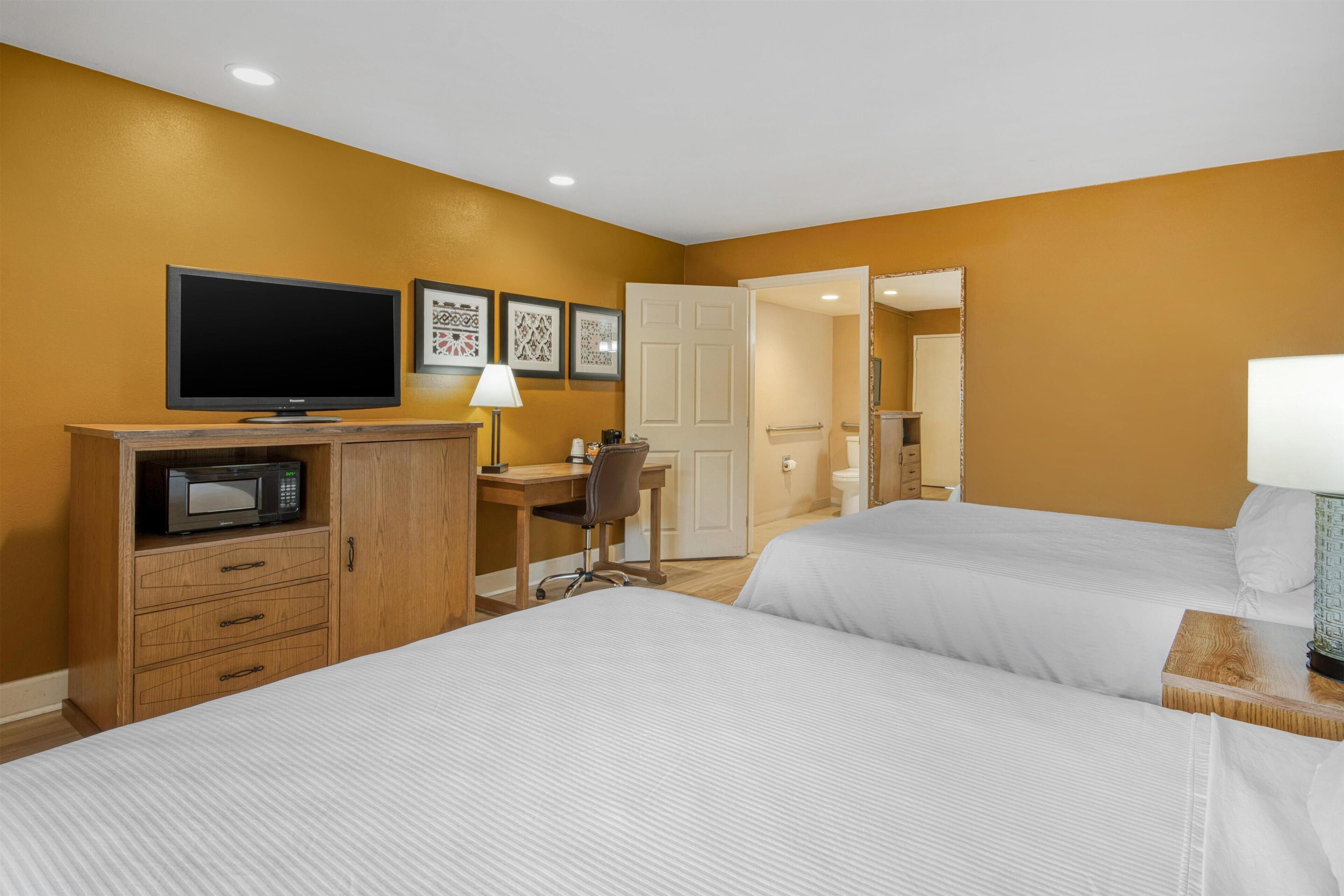 Habitación de hotel con dos camas, un escritorio con silla, televisión, microondas y cuadros en la pared.