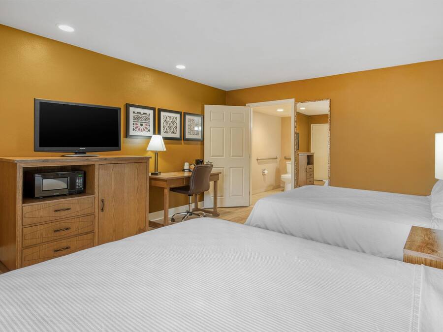 Habitación de hotel con dos camas, un escritorio con silla, televisión, microondas y cuadros en la pared.