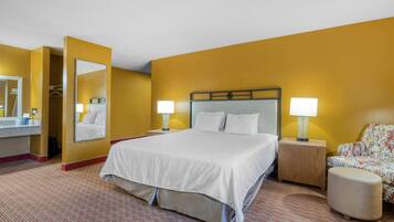Una habitación de hotel con una cama grande, dos mesitas de noche con lámparas, un espejo, una silla y un pequeño reposapiés.