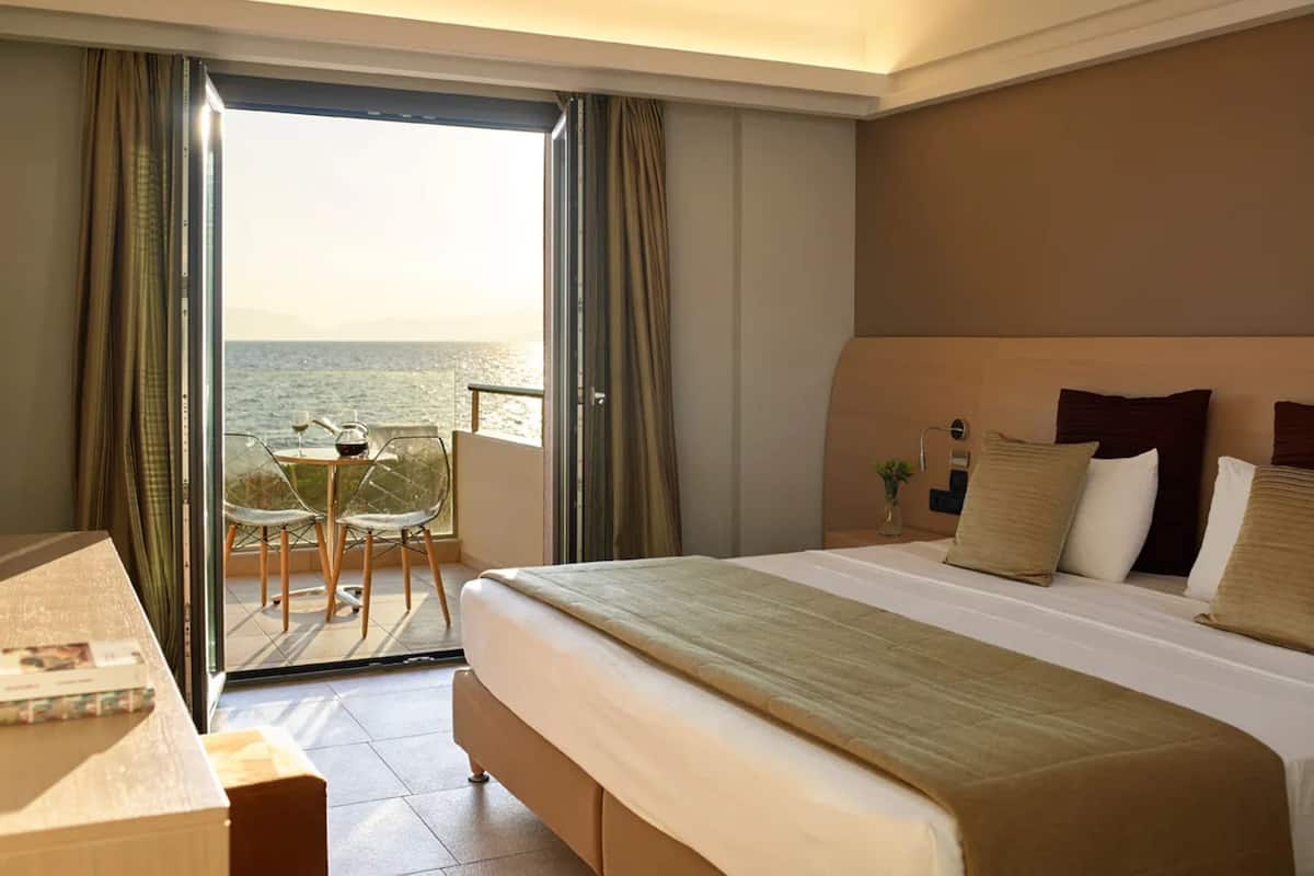 A hotel room with a bed, a desk, a chair, and a view of the sea.