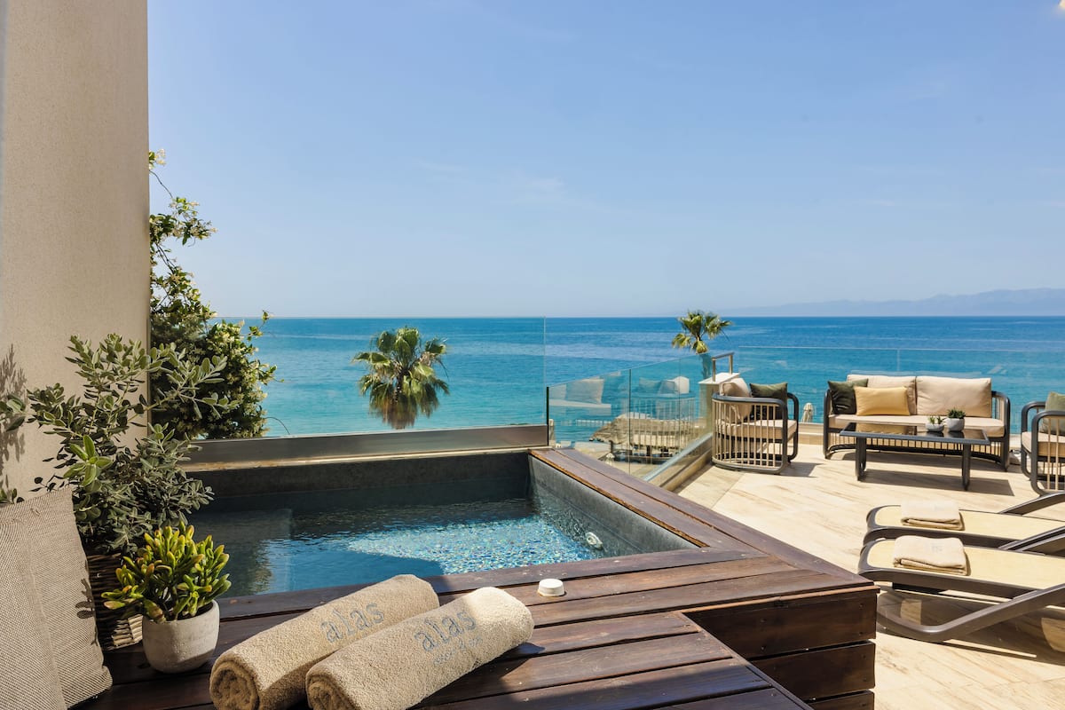 A rooftop pool area with a view of the sea, a wooden deck, lounge chairs, and potted plants.