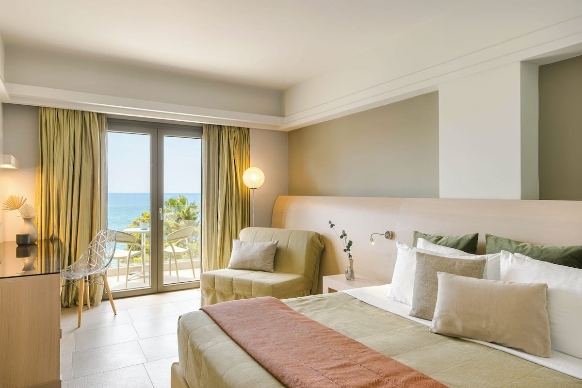 A hotel room with a bed, a desk, a chair, and a view of the ocean through a sliding door.