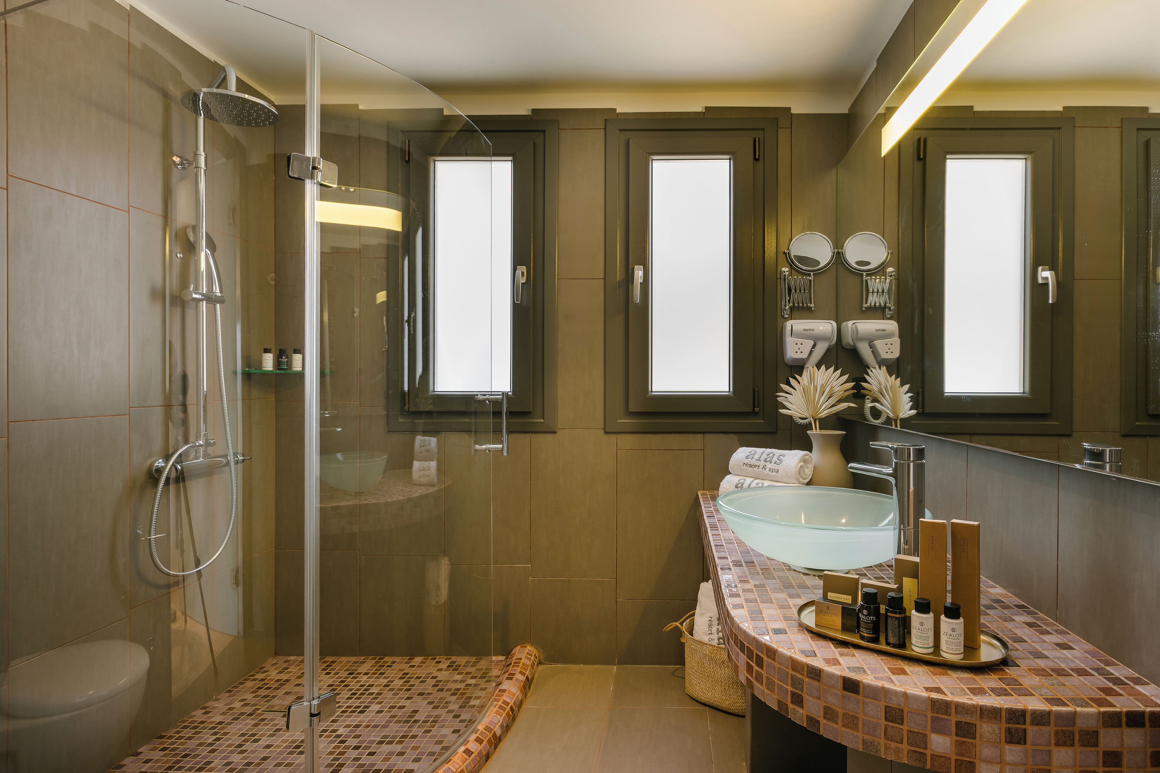 Un baño moderno con ducha envuelta en vidrio, lavamanos con espejo y artículos de aseo en la encimera.
