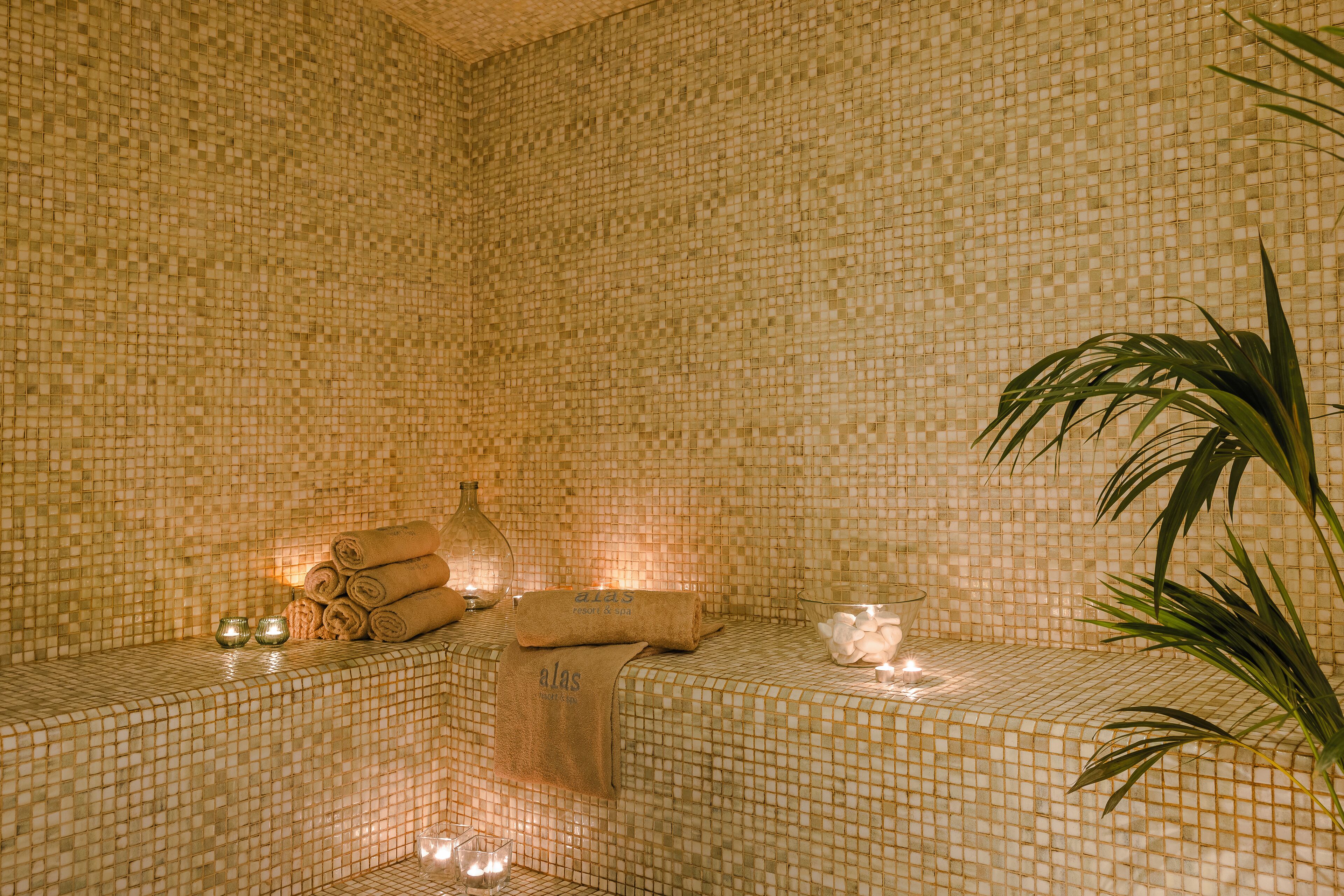 Een spa-ruimte met mozaïektegels, een massagetafel, handdoeken, kaarsen en een plant.