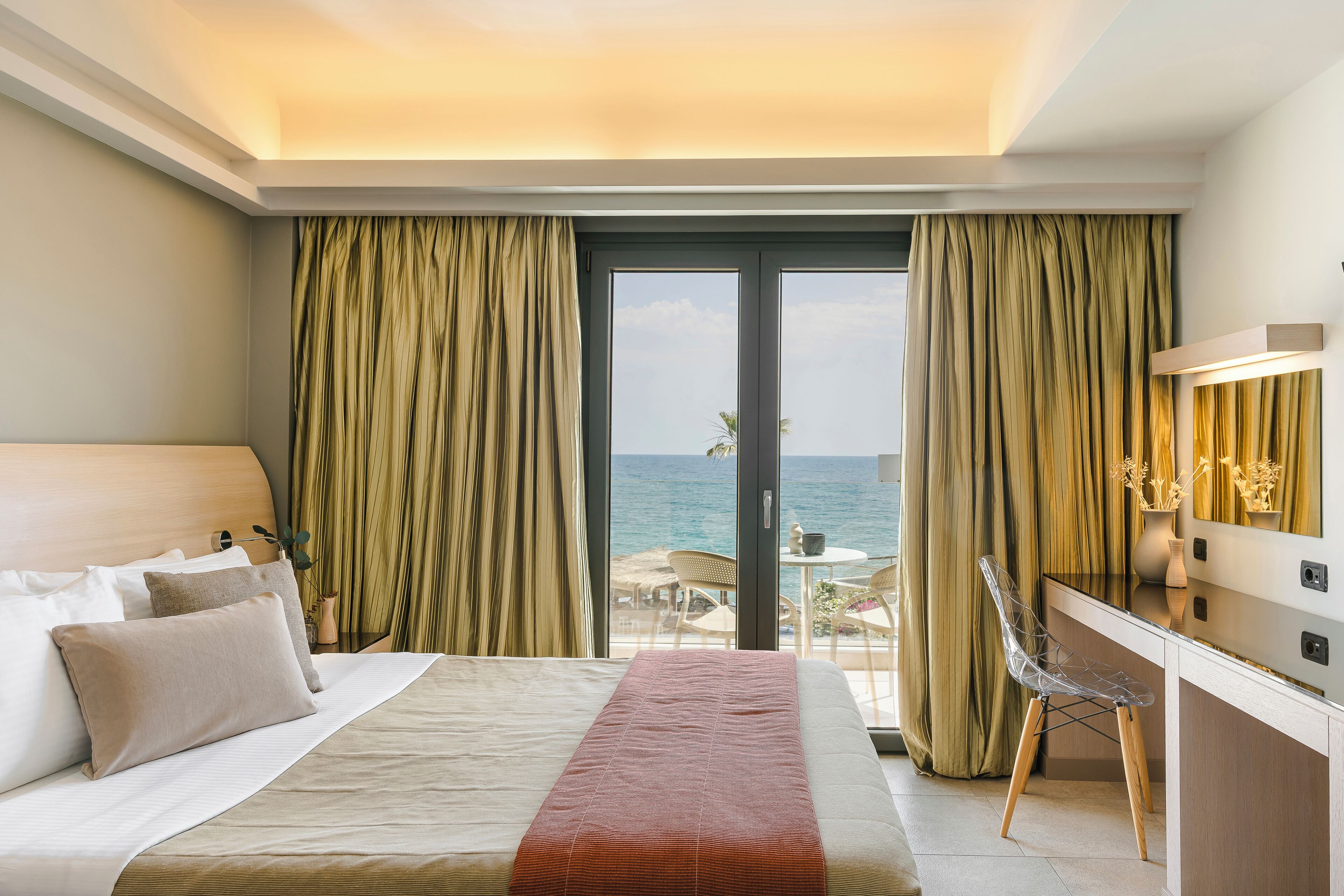 A hotel room with a bed, a desk, and a view of the sea.