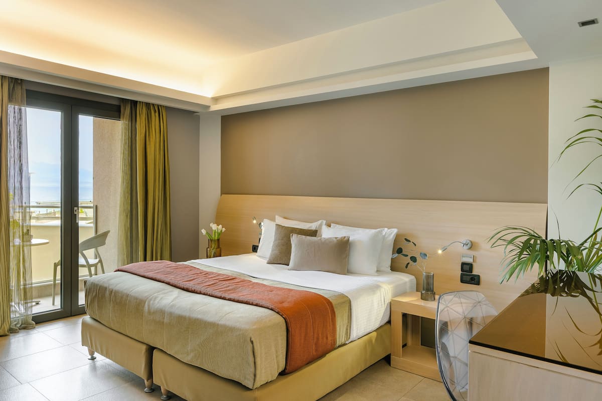 A hotel room with a large bed, a desk, a chair, and a view of the outdoors.