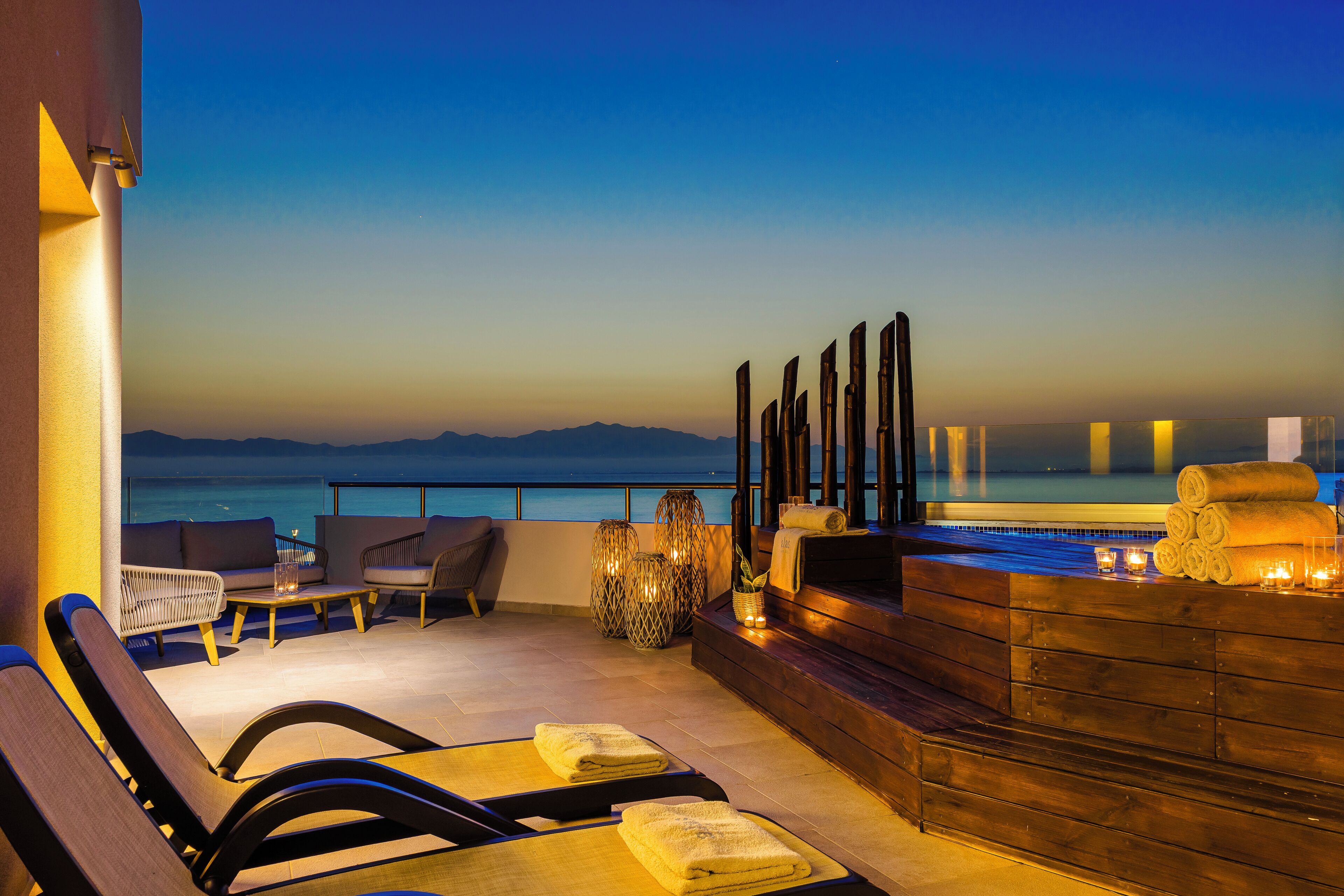 Une terrasse avec vue sur la mer, des meubles en bois et un coin salon avec des coussins.