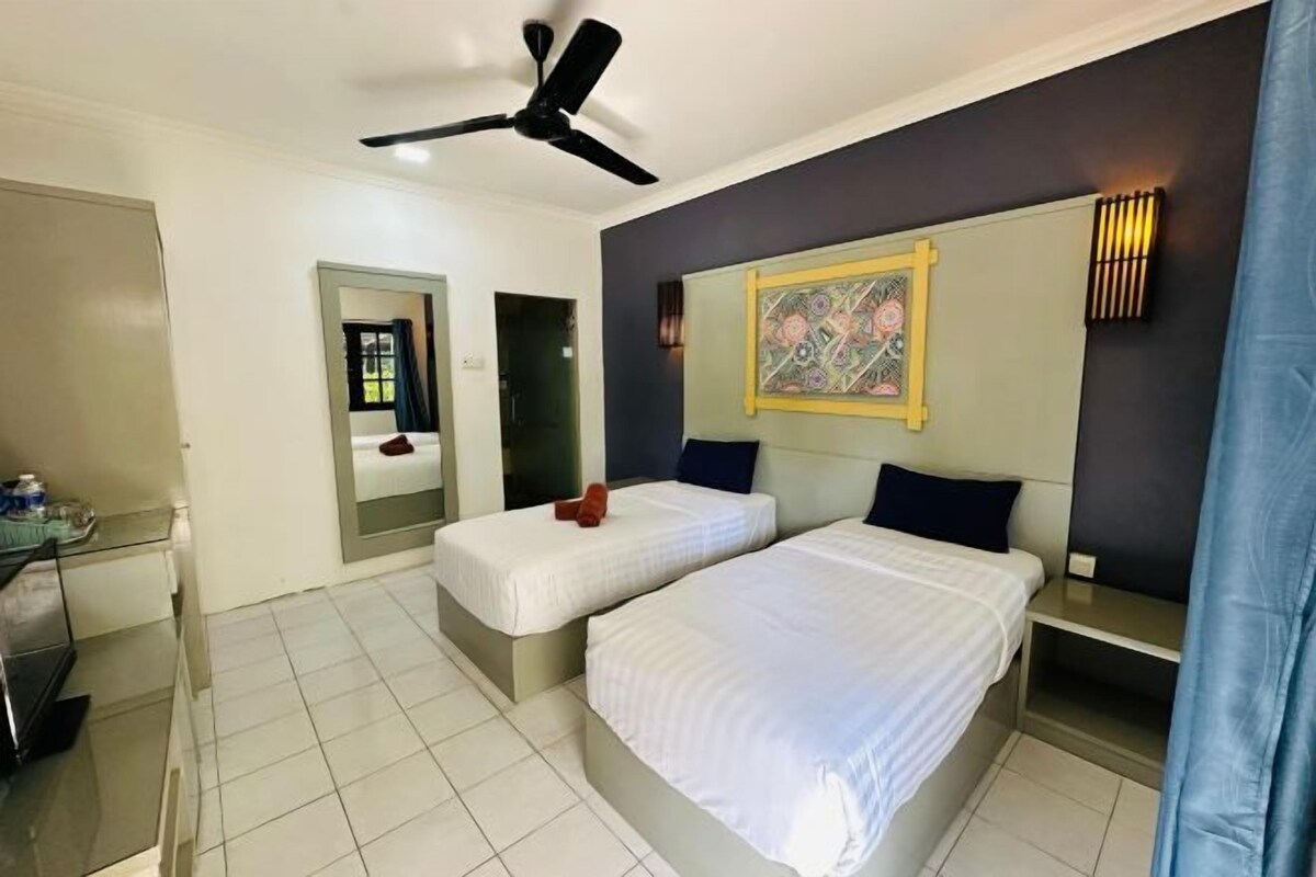 A hotel room with two beds, a ceiling fan, a small table, a mirror, and a wall-mounted light fixture.