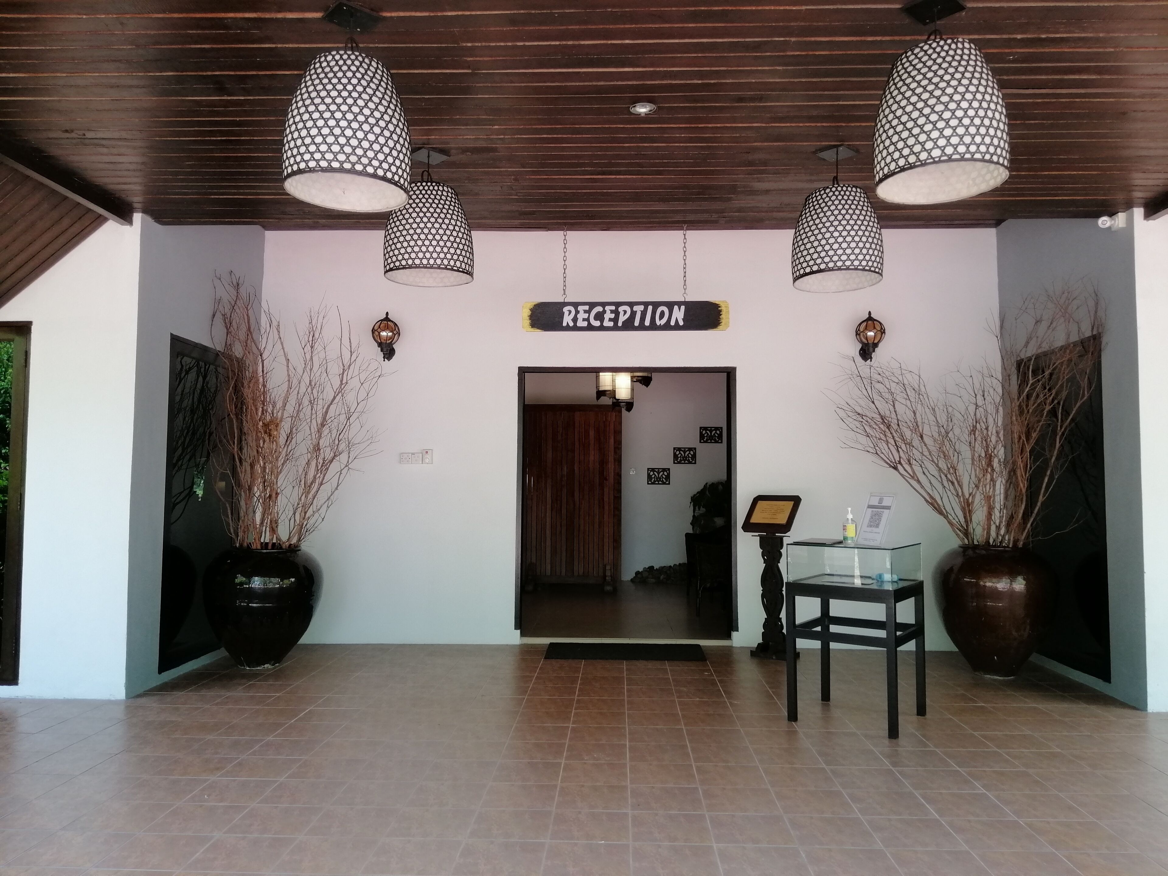 A reception area with a wooden ceiling, two large hanging lamps, a reception desk, and potted plants.