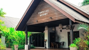 Eingang eines tropischen Resorts mit Holzfassade und einem Schild mit der Aufschrift 'Tropical Resort'.