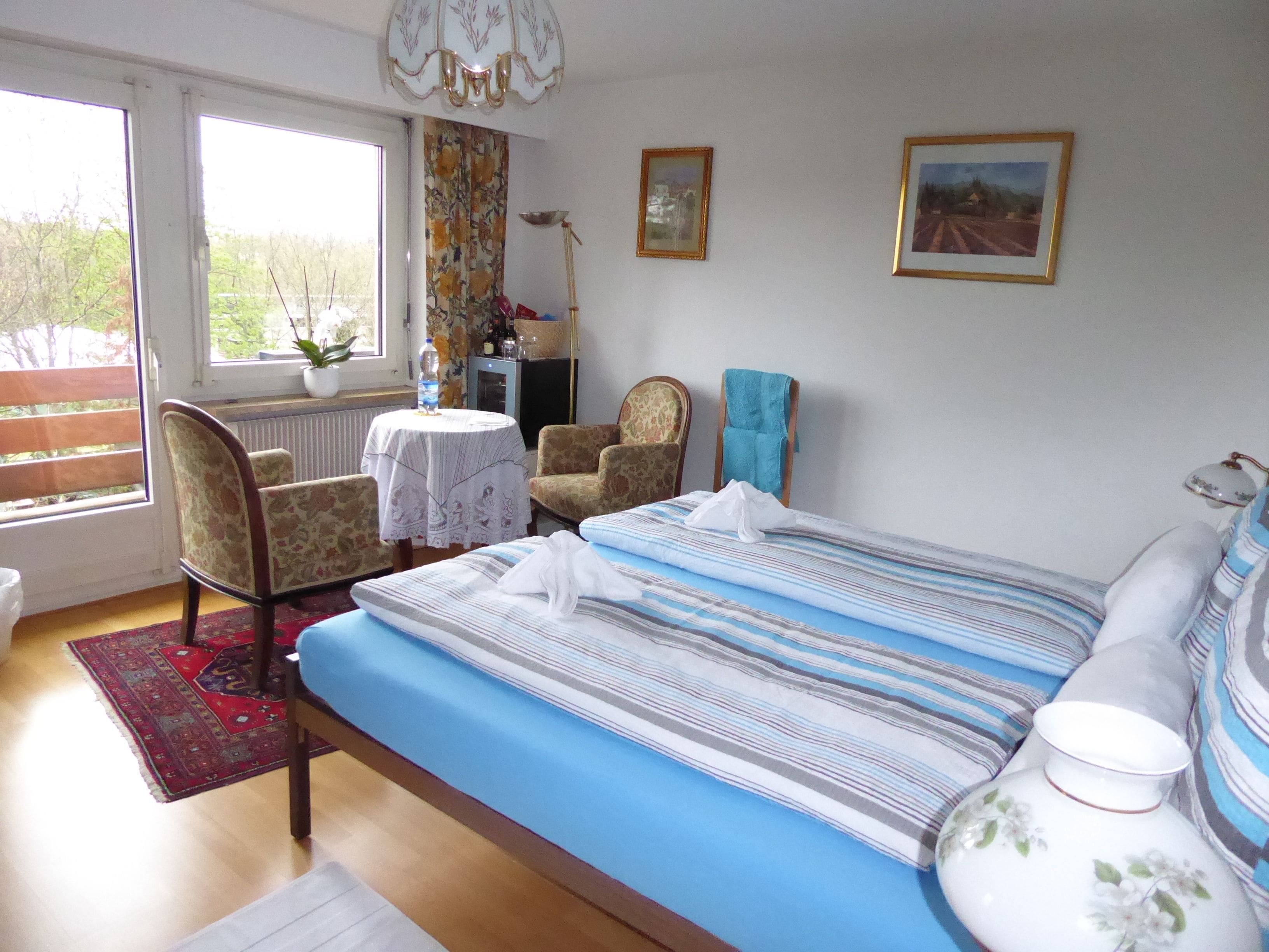 Un dormitorio con una cama, dos sillones, una mesa, un radiador y dos cuadros en la pared.