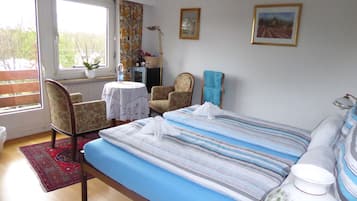 Un dormitorio con una cama, dos sillones, una mesa, un radiador y dos cuadros en la pared.