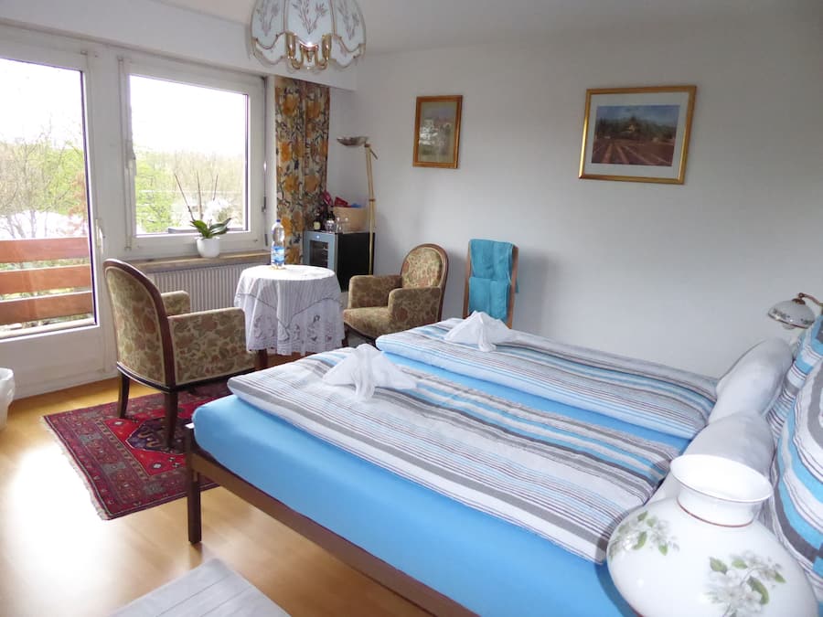 Un dormitorio con una cama, dos sillones, una mesa, un radiador y dos cuadros en la pared.