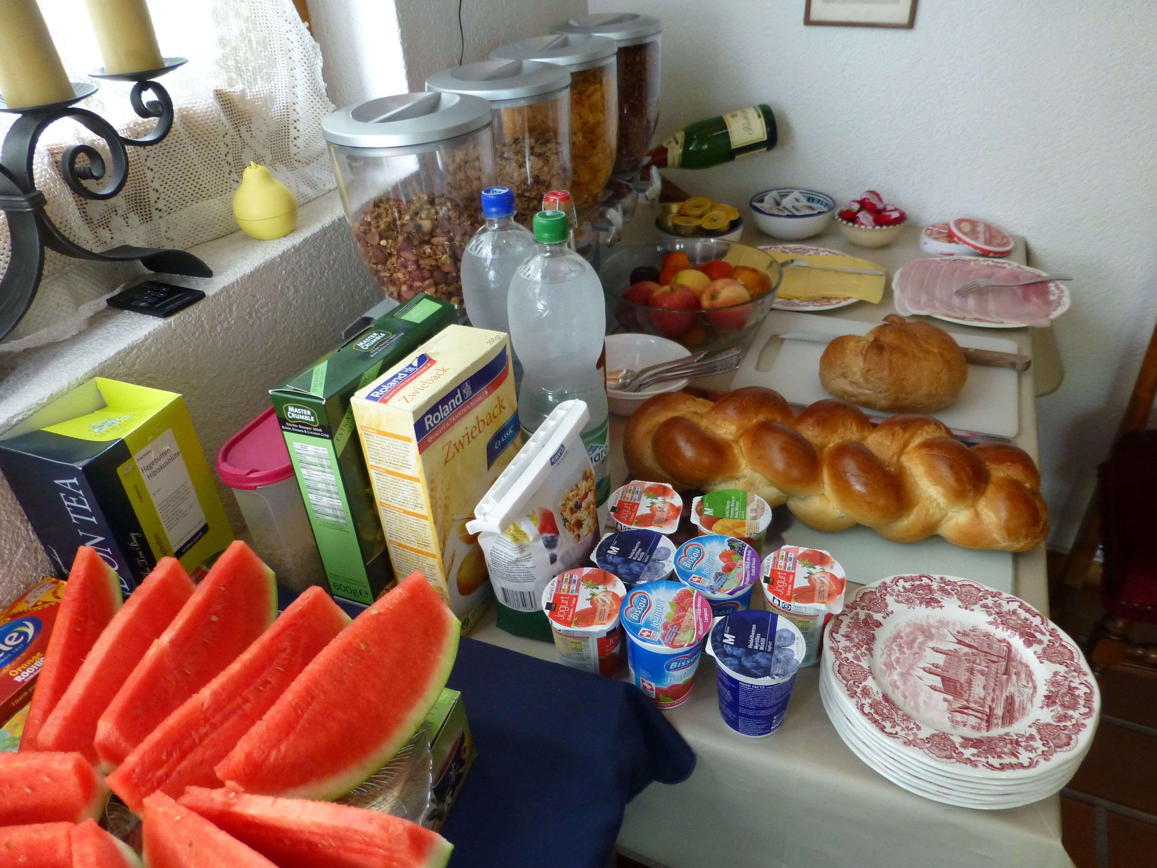 Un bufé de desayuno con diversos alimentos y bebidas, incluyendo pan, frutas y productos lácteos.