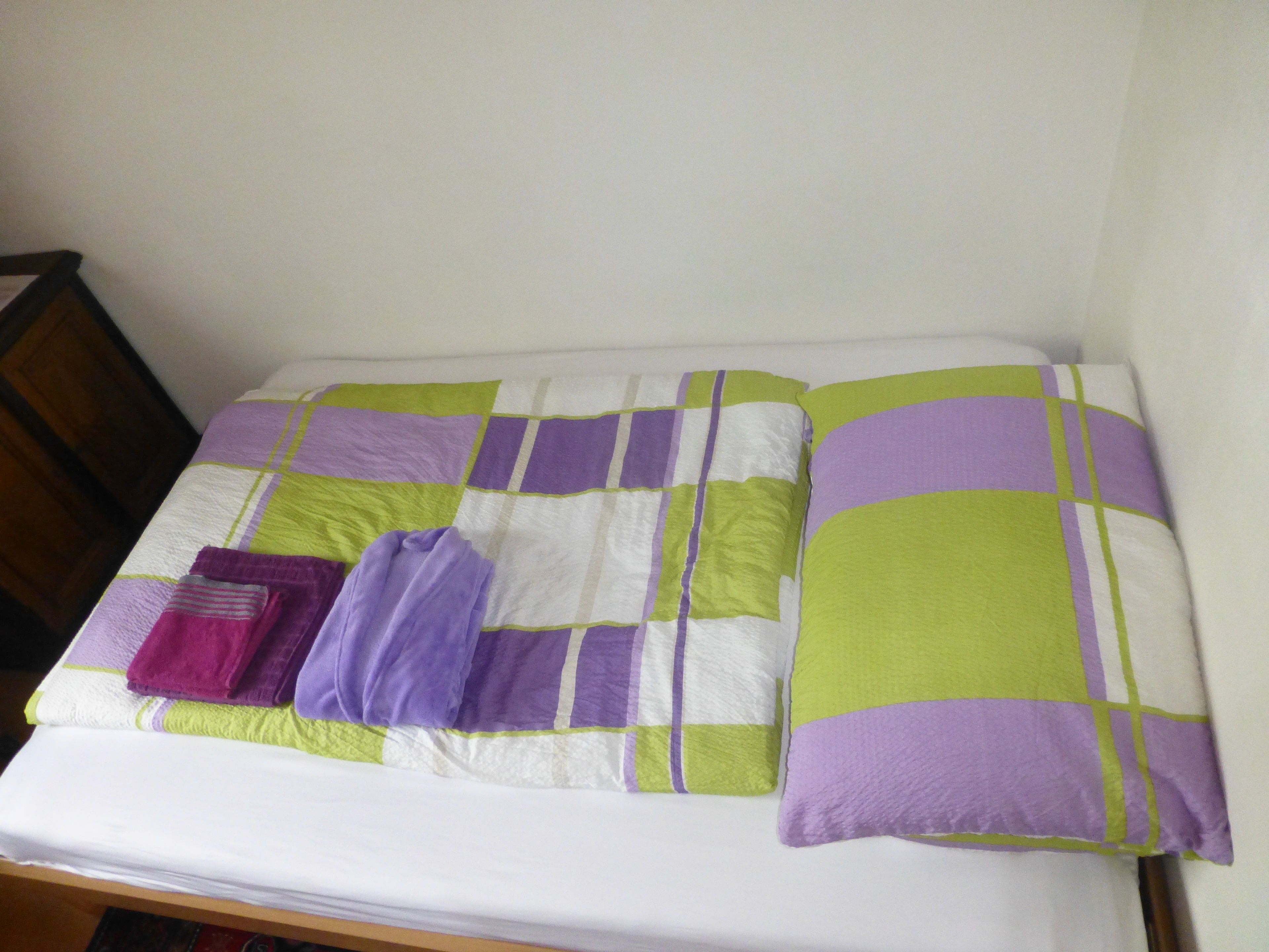 Una cama con un edredón verde y morado, una almohada morada y una manta morada doblada.