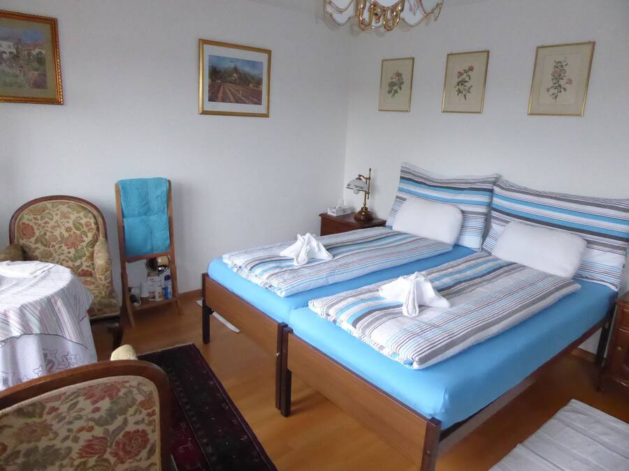 Een keurig opgeruimde slaapkamer met een groot bed, een stoel, een klein tafeltje en een nachtkastje.