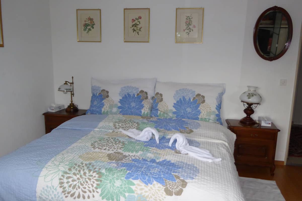 A neatly made bed with floral bedding, two white towels, and a bedside table with a lamp.