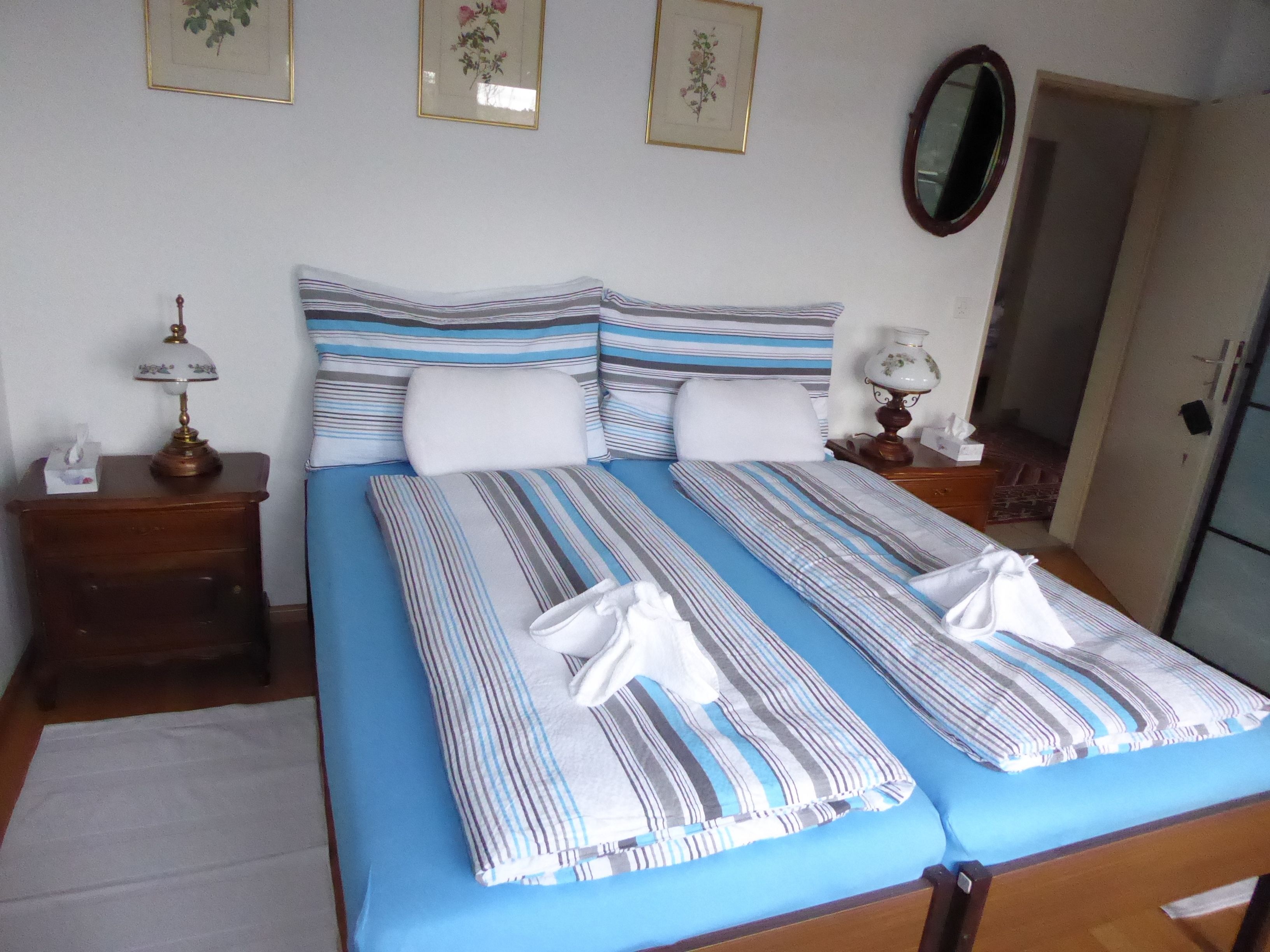 Una cama bien hecha con ropa de cama a rayas, una mesita de noche con lámpara y cuadros con motivos florales en la pared.