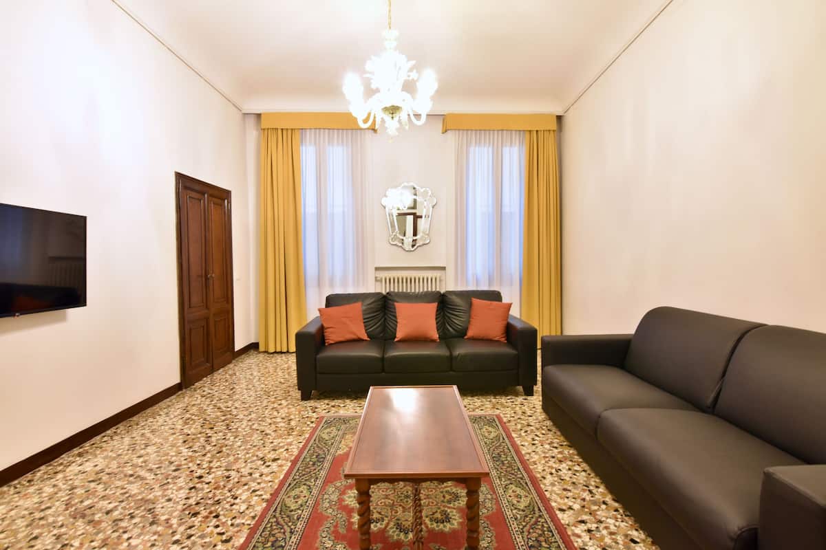 A living room with a dark sofa, a wooden coffee table, a television, and a patterned carpet.