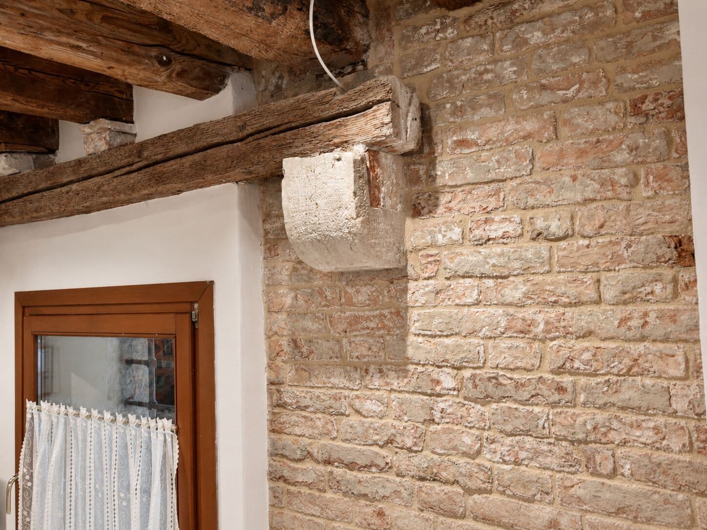 A rustic interior with exposed wooden beams, a brick wall, and a wooden door.