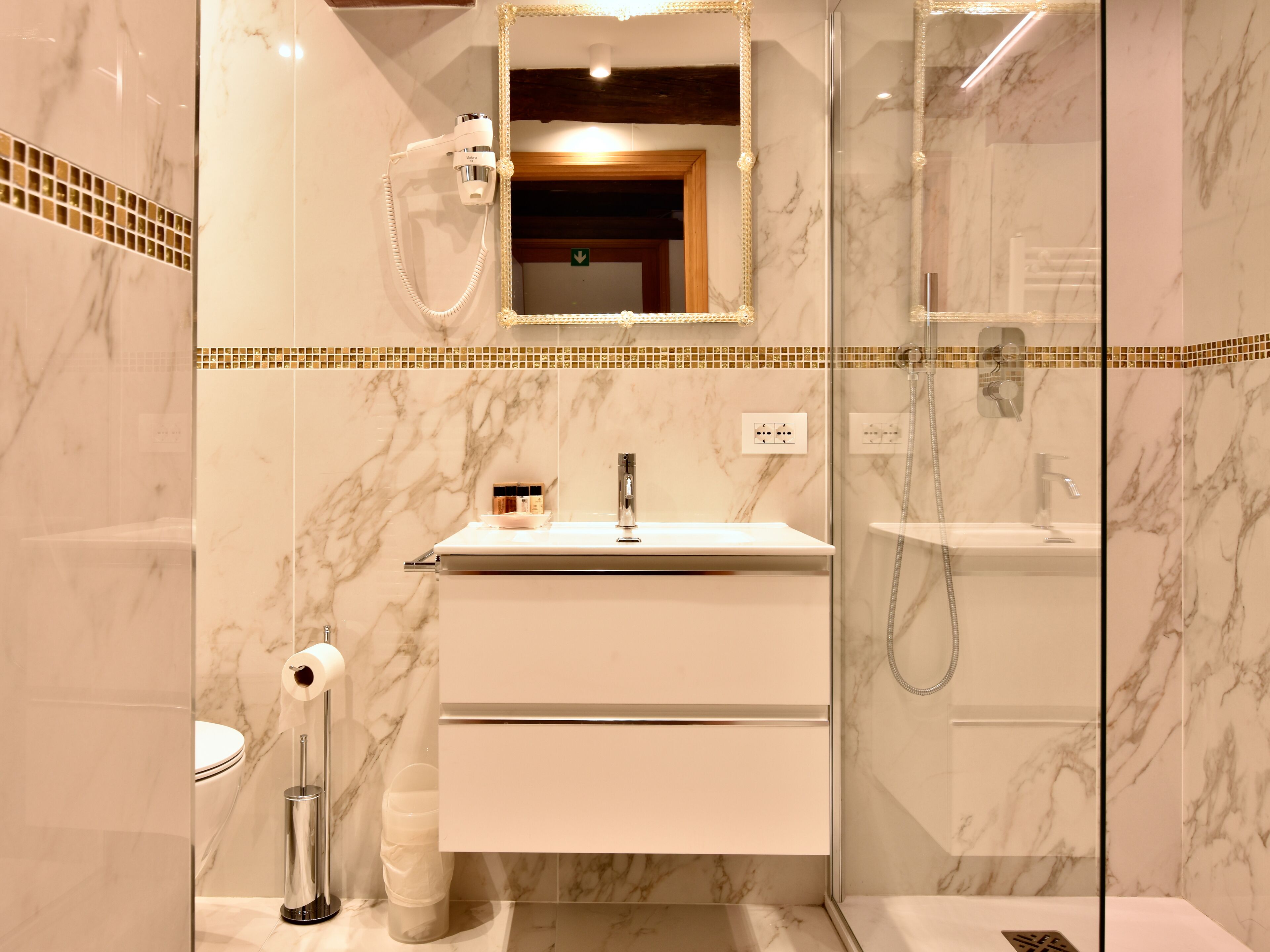 Un bagno moderno con doccia vetrata, parete rivestita in marmo, mobile lavabo bianco con specchio e WC.