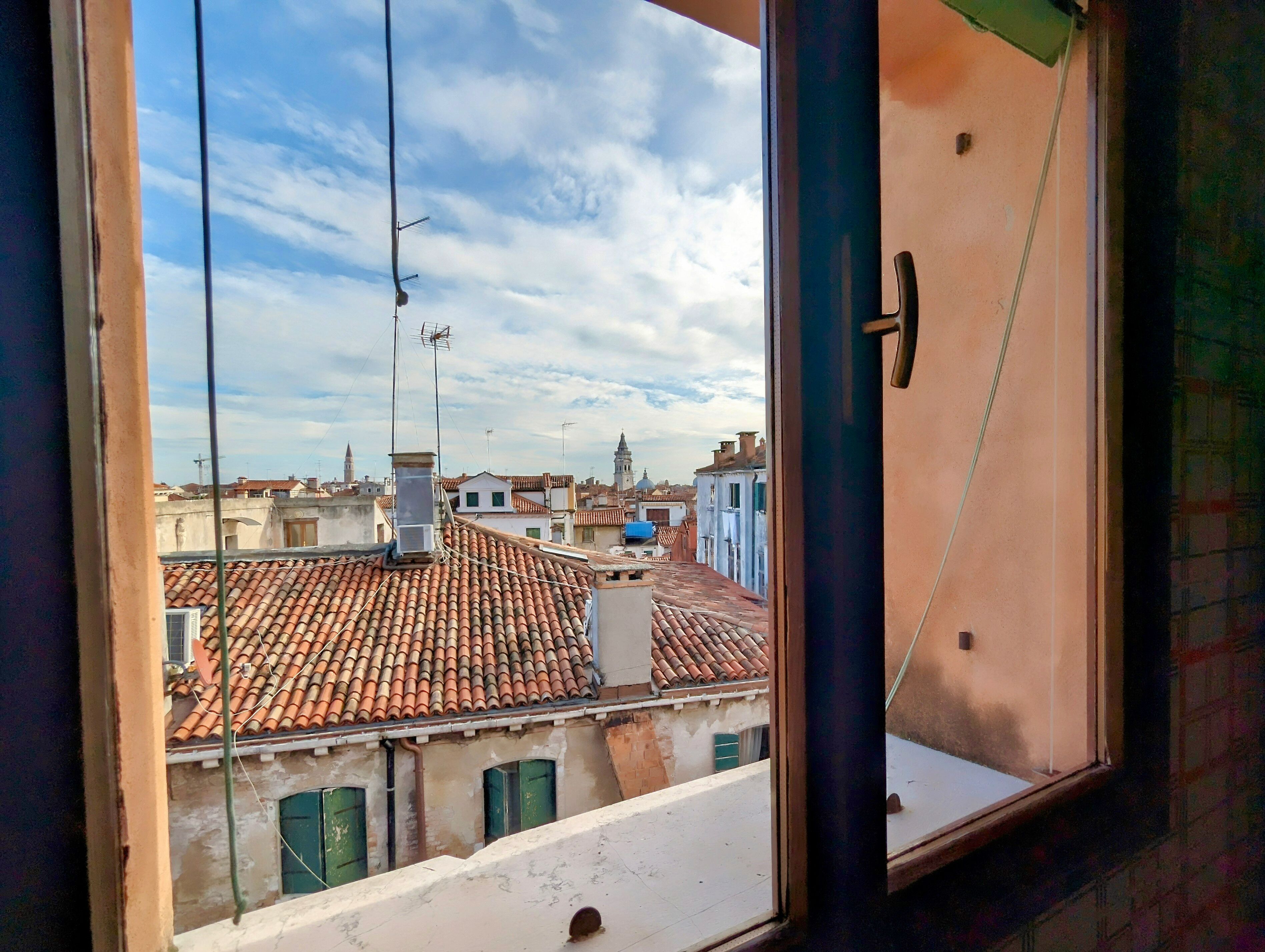 A view from a window overlooking a cityscape with terracotta-tiled rooftops and a clear sky.