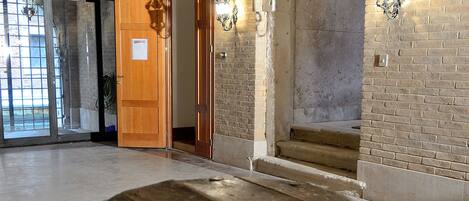 A stone well with a wooden lid in a spacious, open hall with exposed wooden beams and brick walls.