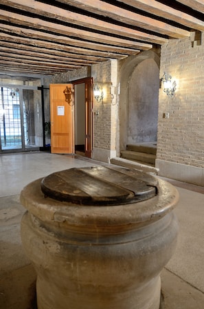 A stone well with a wooden lid in a spacious, open hall with exposed wooden beams and brick walls. - Da Bruno Homes (Venice)