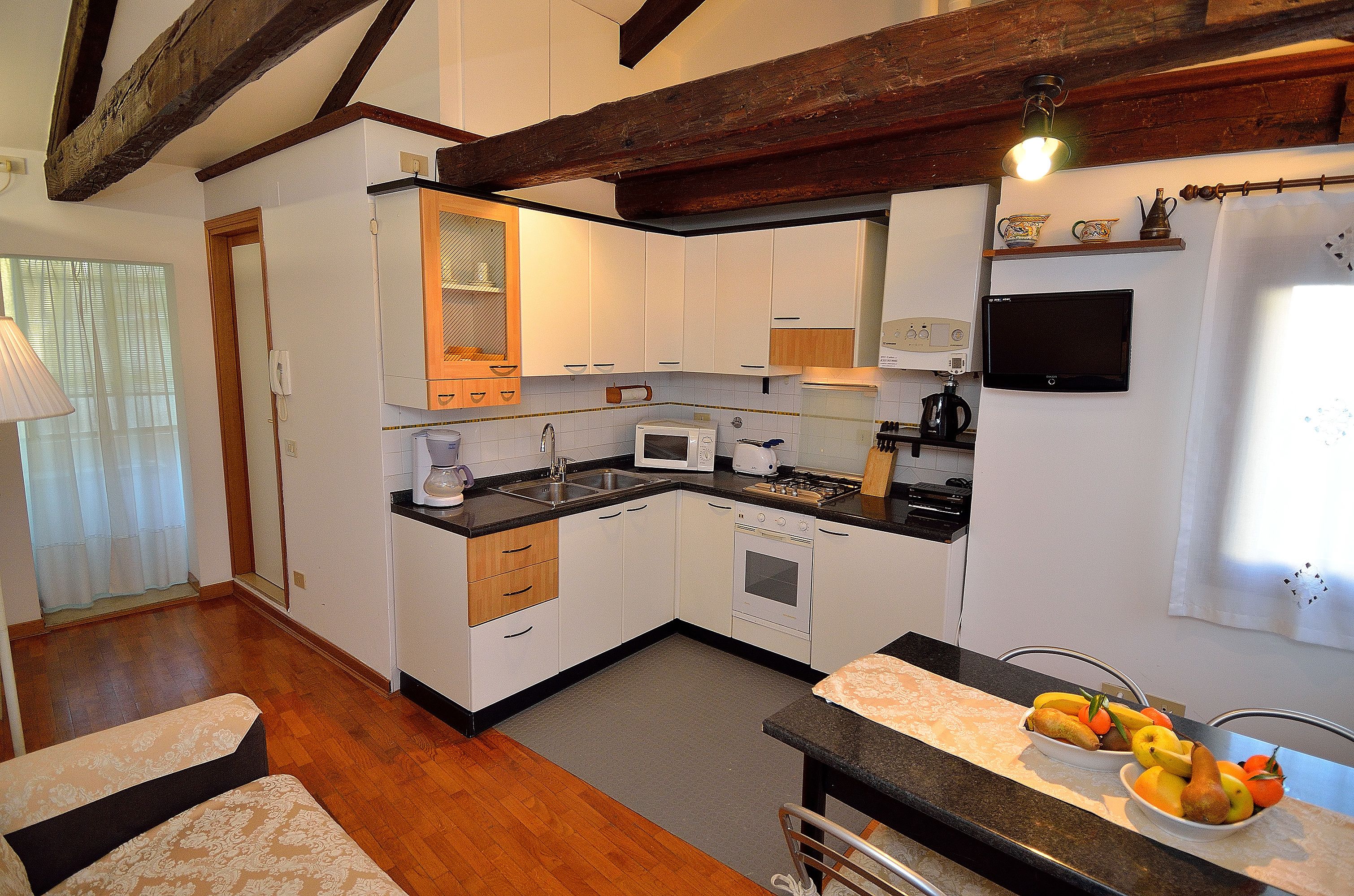 A compact kitchen with white cabinets, a microwave, a coffee maker, and a fruit bowl on the counter.