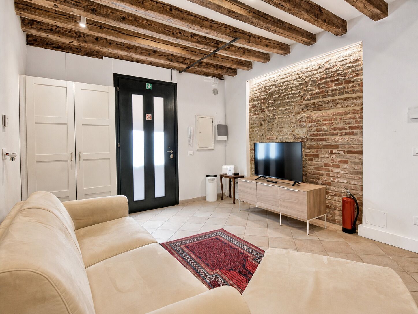 Un salon moderne avec un canapé, un tél éviseur posé sur un meuble en bois, un mur en briques et une porte avec une enseigne.