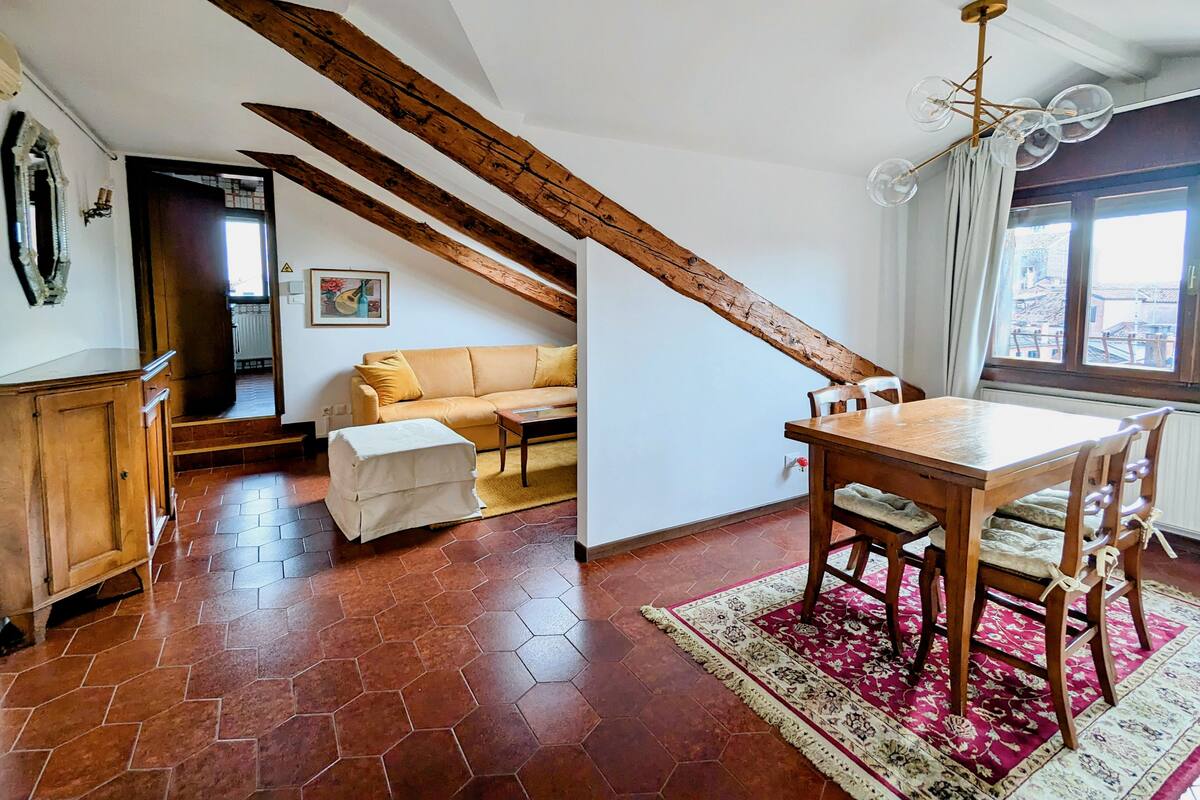 A room with a wooden ceiling, a sofa, a dining table, and a window with a view.