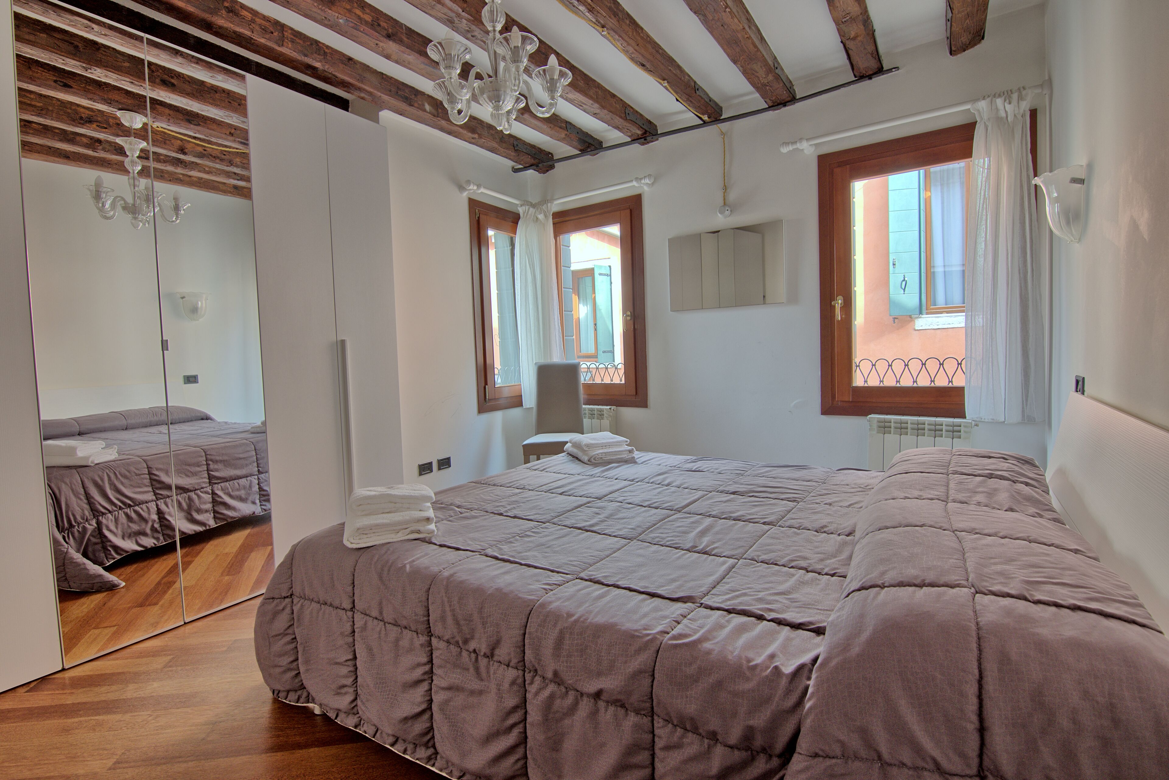 A bedroom with a large bed, a mirror, a chandelier, and a window with a view.